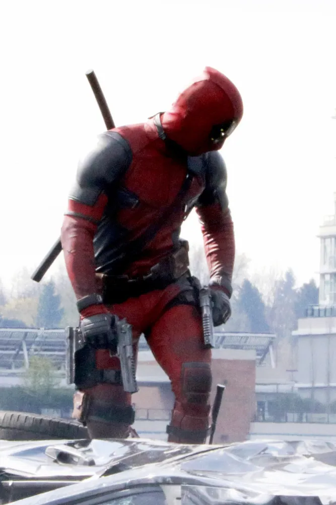 Deadpool em seu traje vermelho e preto, fazendo um sinal de coração com as mãos para a câmera.