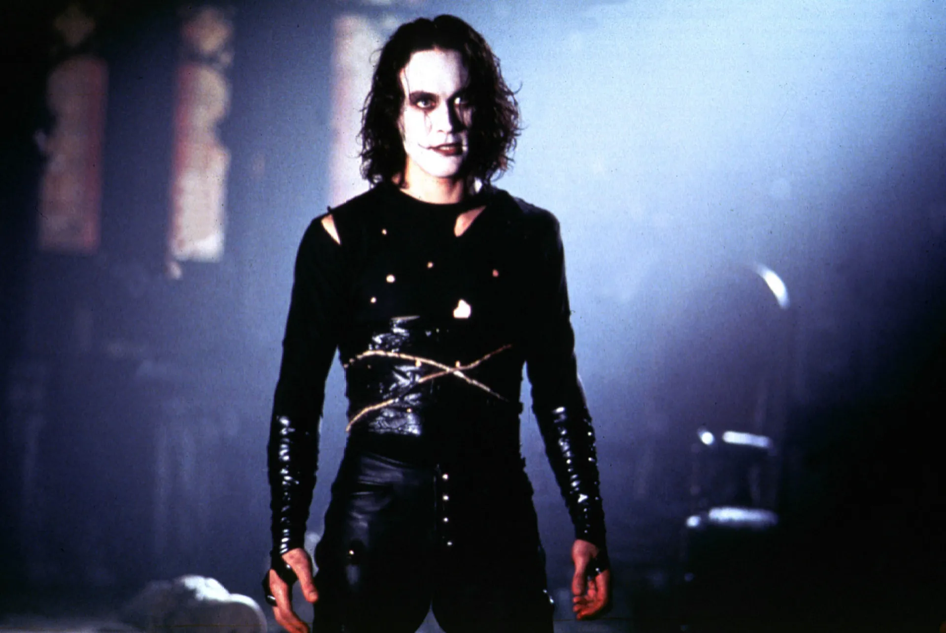 Eric Draven como O Corvo, com sua maquiagem icônica de palhaço triste e roupas pretas.