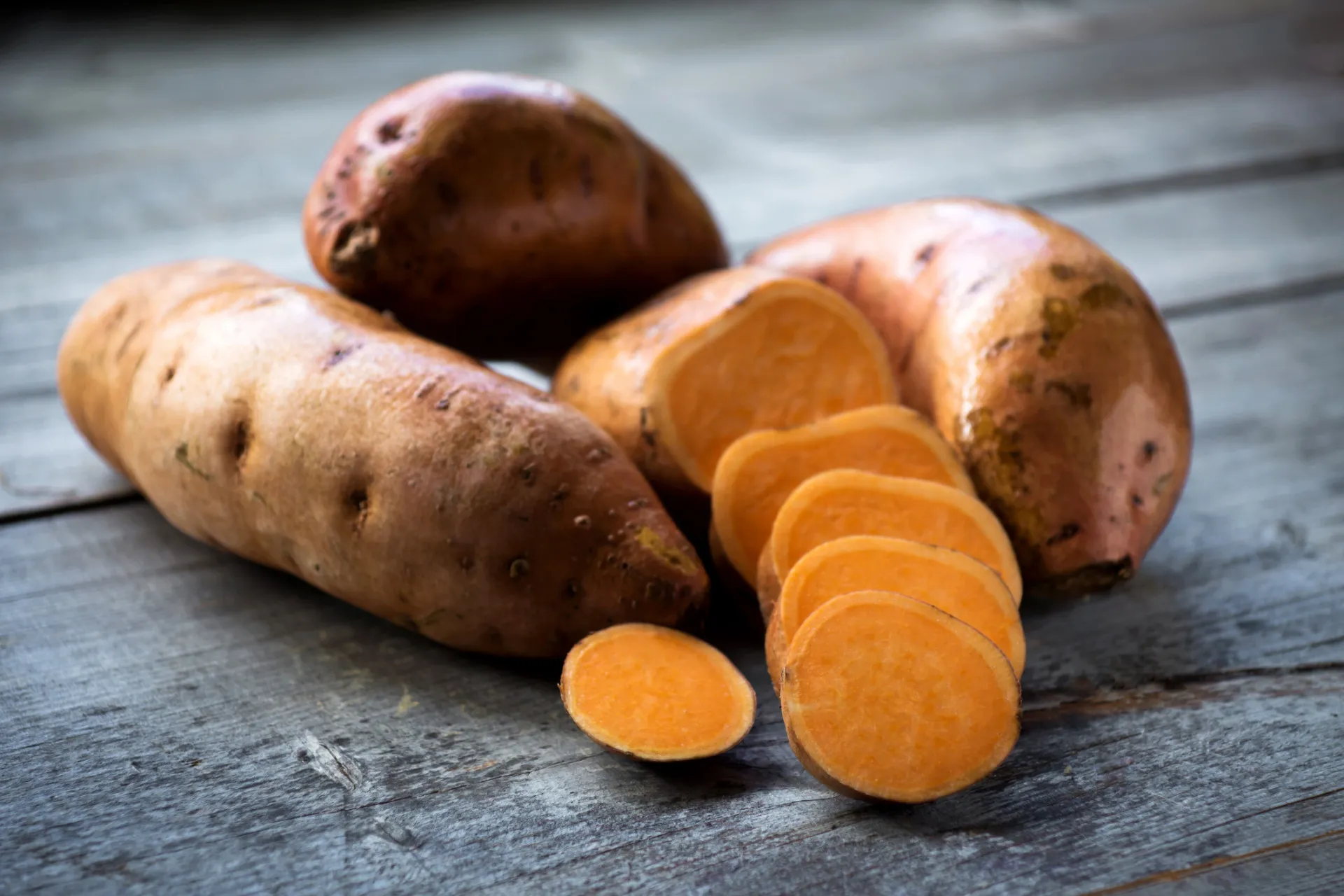 Batatas-doces inteiras e cortadas, mostrando sua polpa laranja.