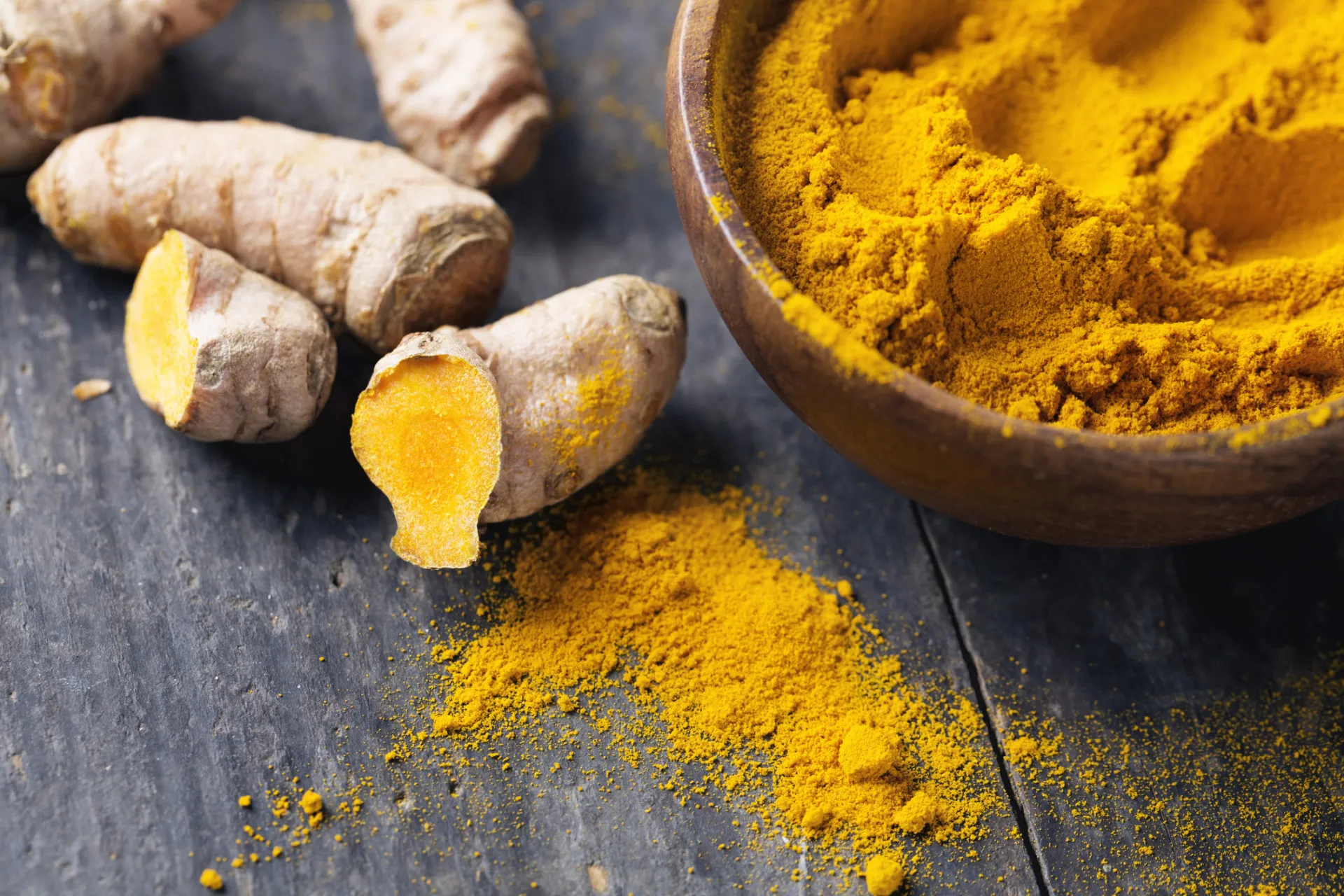 Pó de cúrcuma amarelo-alaranjado e a raiz fresca.