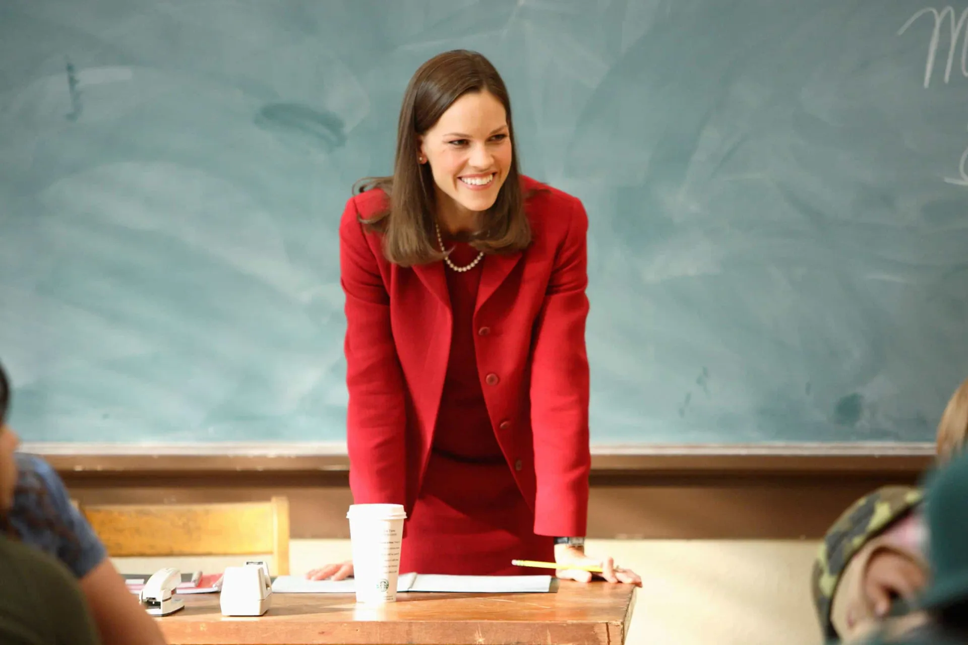 Hilary Swank como a professora Erin Gruwell, rodeada por seus alunos em uma sala de aula.