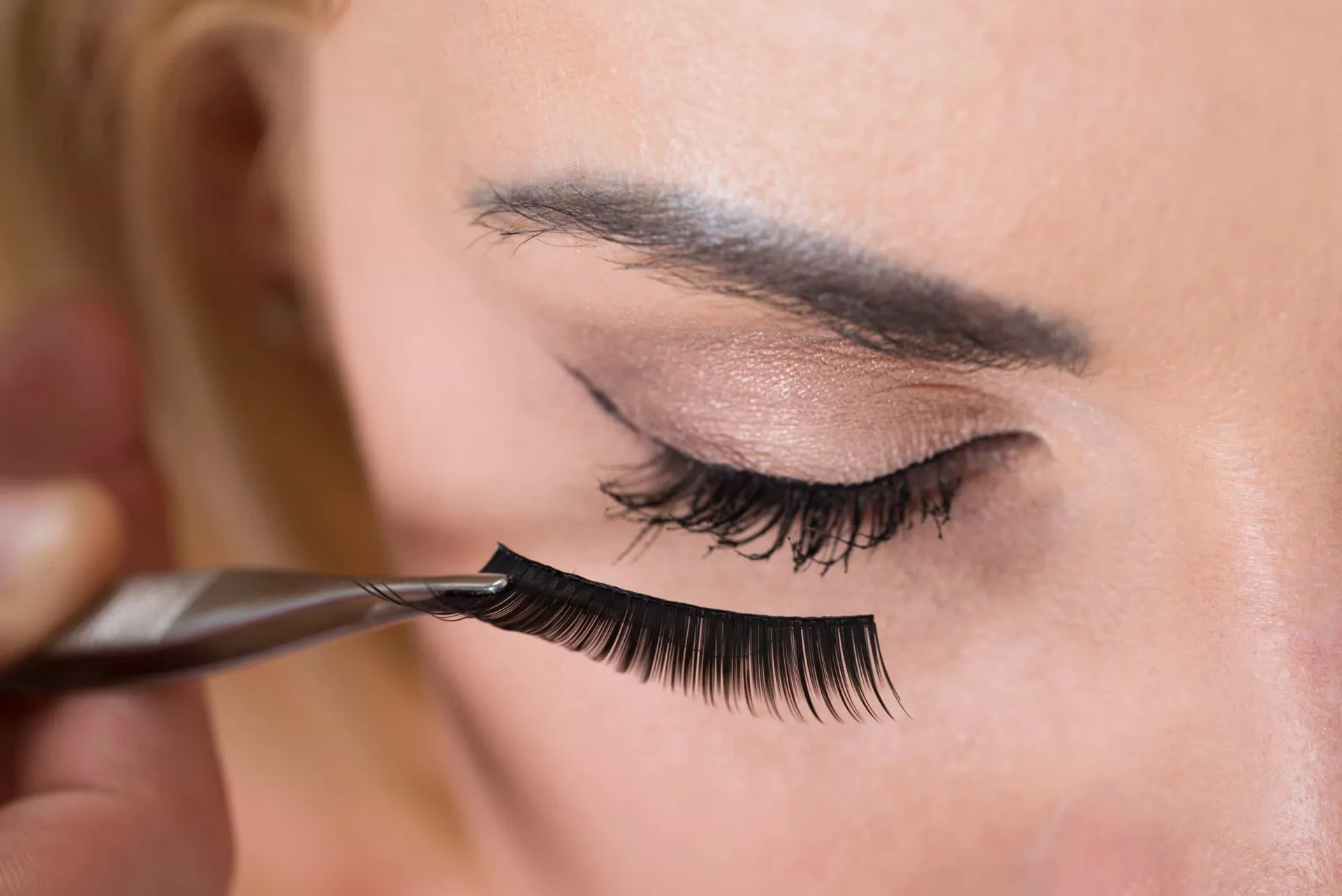 Olho de uma mulher com extensões de cílios, destacando os potenciais riscos do procedimento.