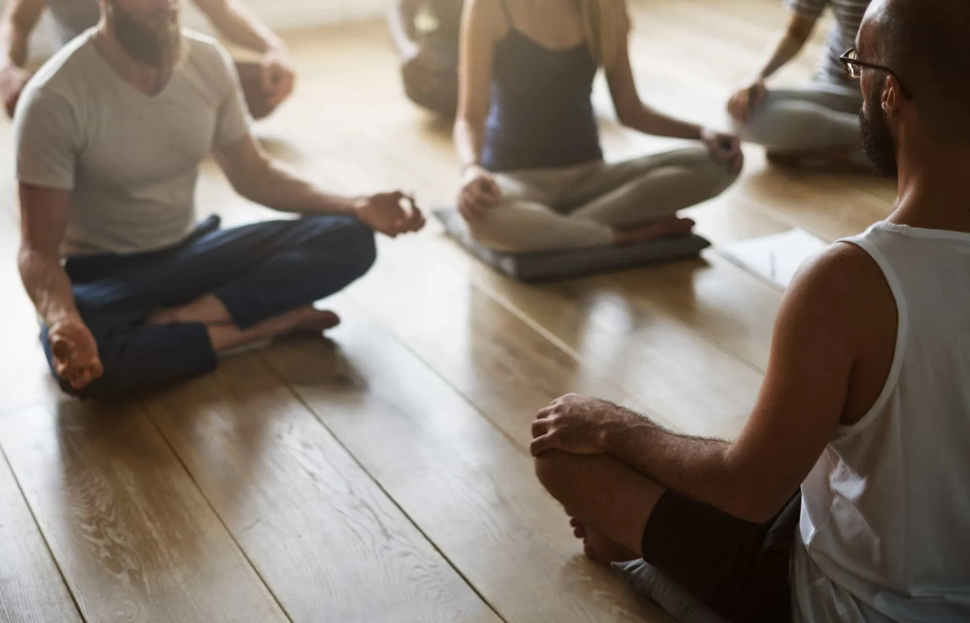 Grupo de pessoas praticando yoga em uma sala iluminada, em posição de meditação.