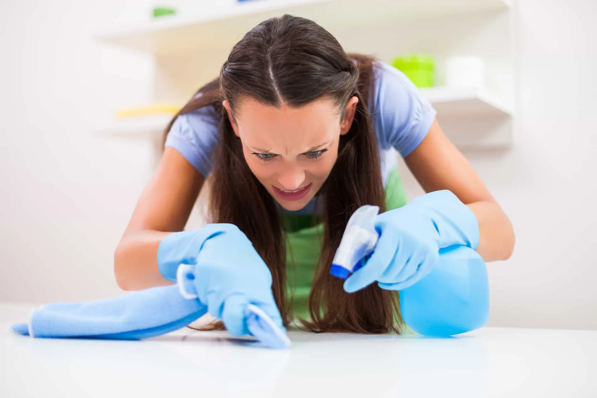 Pessoa usando luvas de borracha e borrifando produto de limpeza em uma superfície.