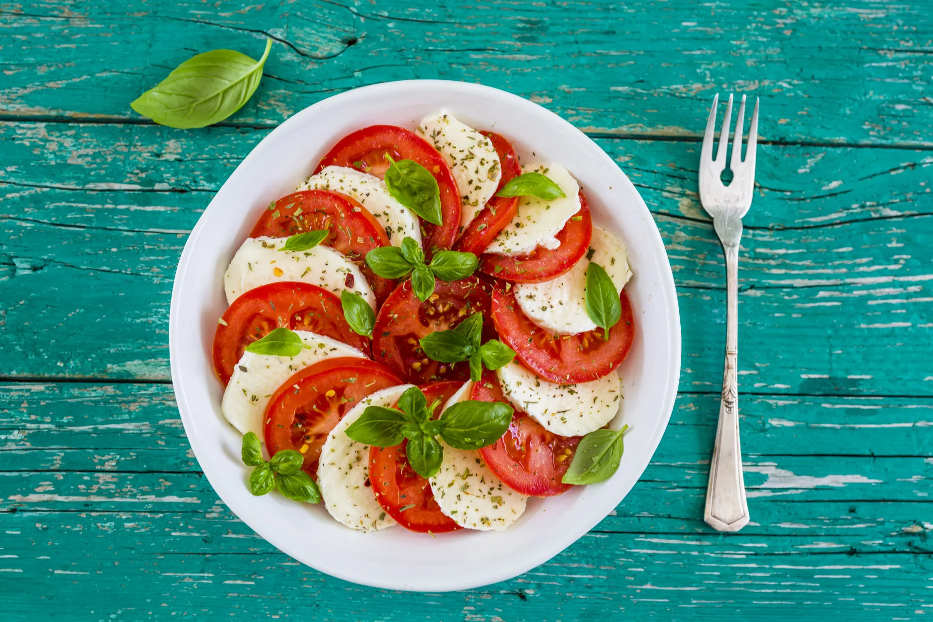 Salada caprese clássica com fatias de tomate, mussarela de búfala e folhas de manjericão.