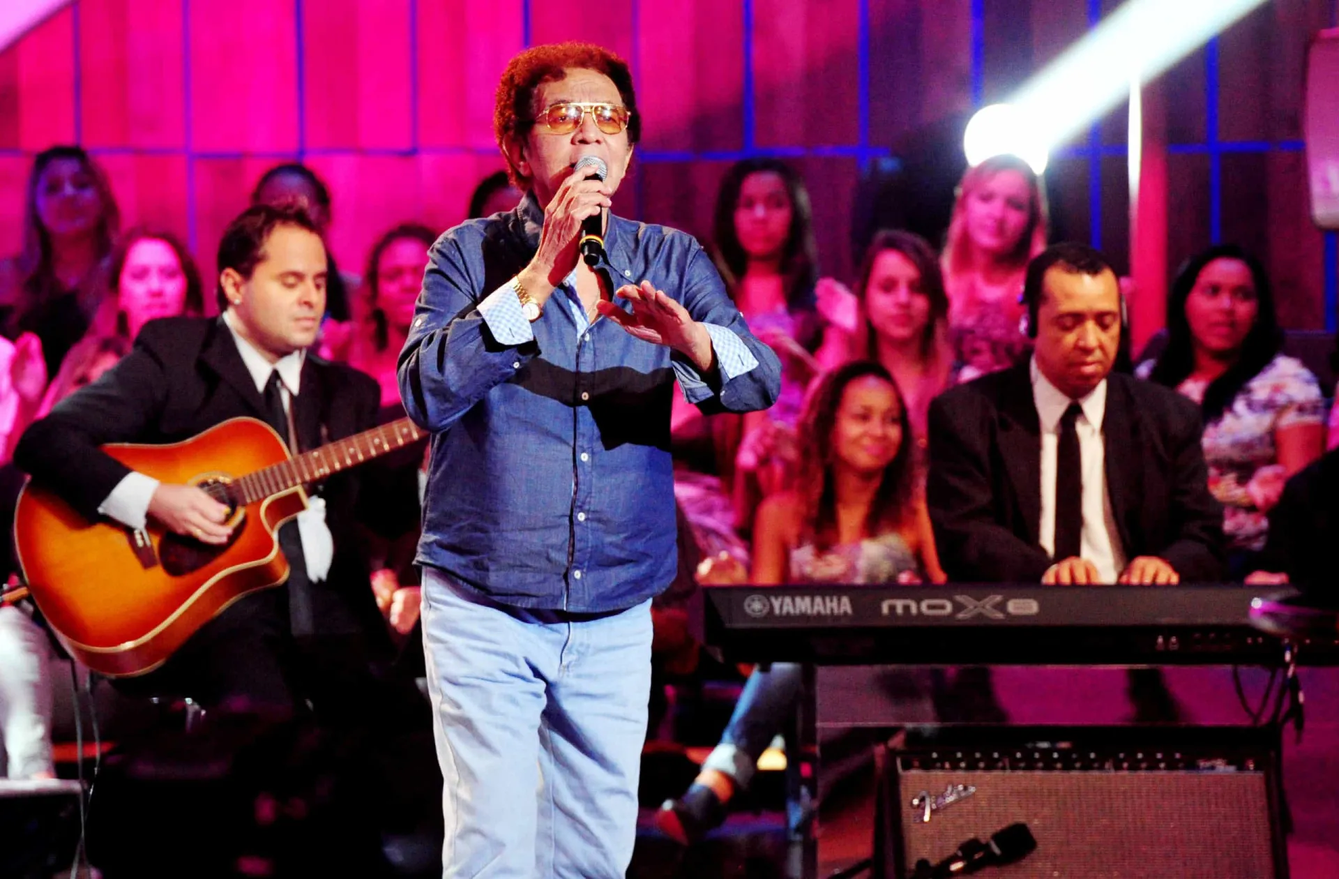 Reginaldo Rossi cantando em um show, com um microfone na mão e expressão emotiva.