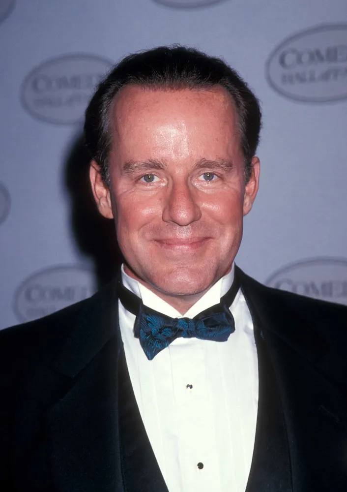 O ator e comediante Phil Hartman sorrindo para a câmera.