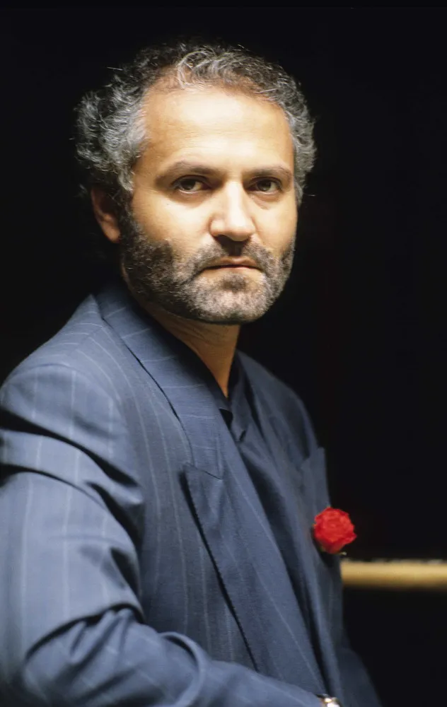 O estilista Gianni Versace com uma expressão séria e elegante.