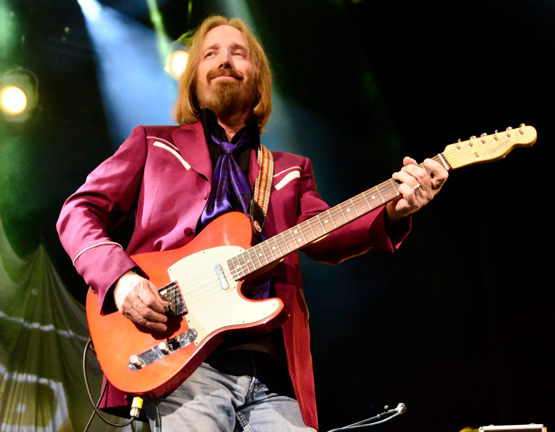O roqueiro Tom Petty cantando em um show, com um olhar concentrado.