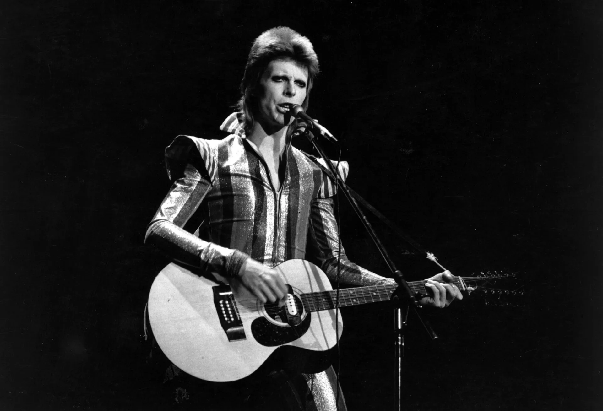 O icônico David Bowie em sua fase Ziggy Stardust, com um visual andrógino e marcante.