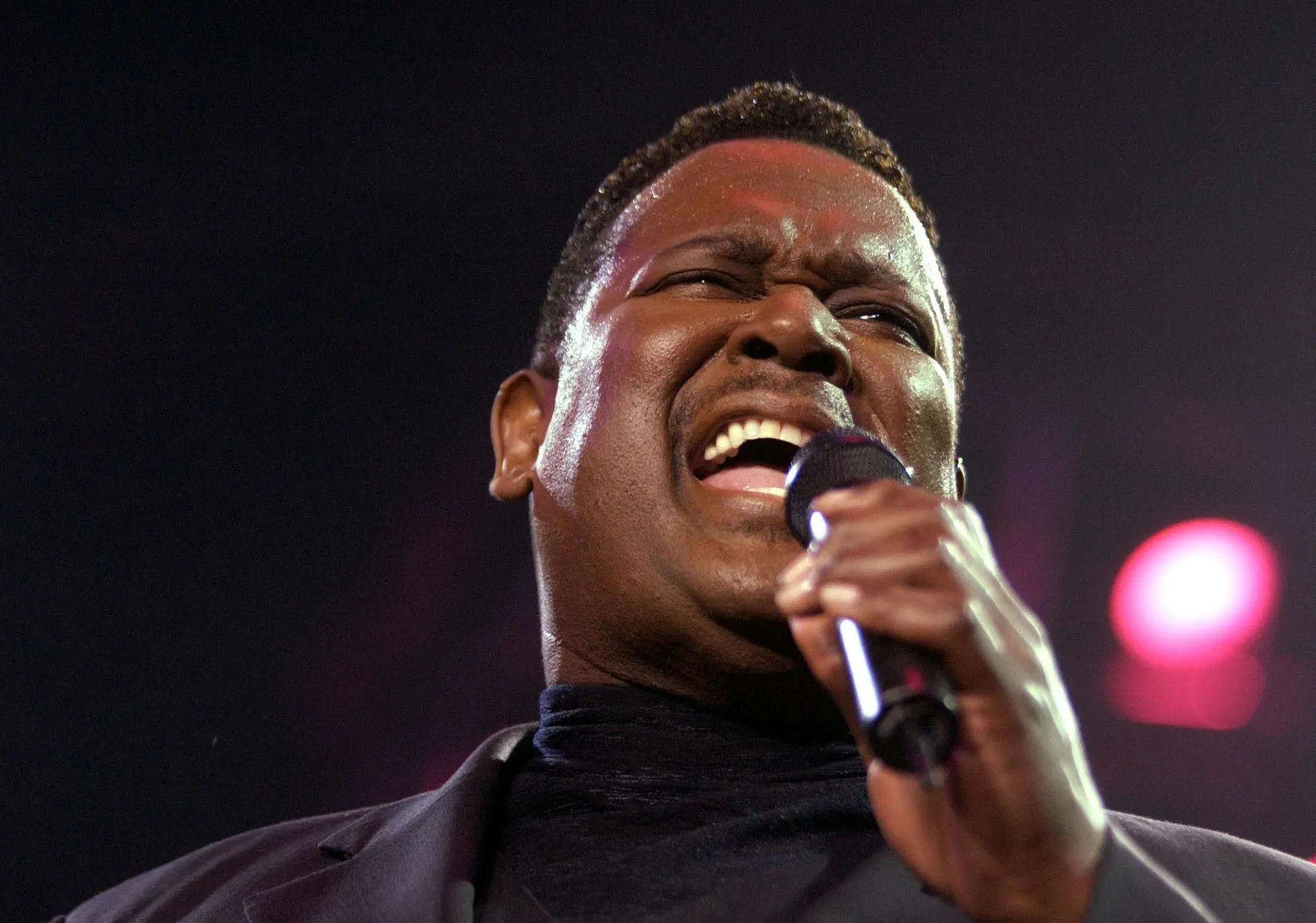 O cantor de R&B Luther Vandross cantando apaixonadamente em um microfone.