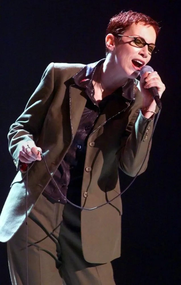 A cantora Annie Lennox, do Eurythmics, com cabelo laranja curto e um terno masculino, um de seus visuais icônicos.