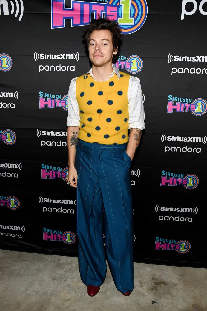 Harry Styles usando um colar de pérolas e esmalte nas unhas, sorrindo para a câmera.