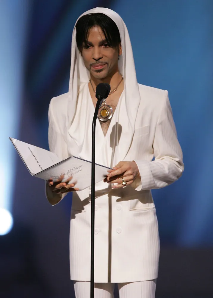 Prince no palco com um visual icônico, usando uma roupa com rendas e babados.