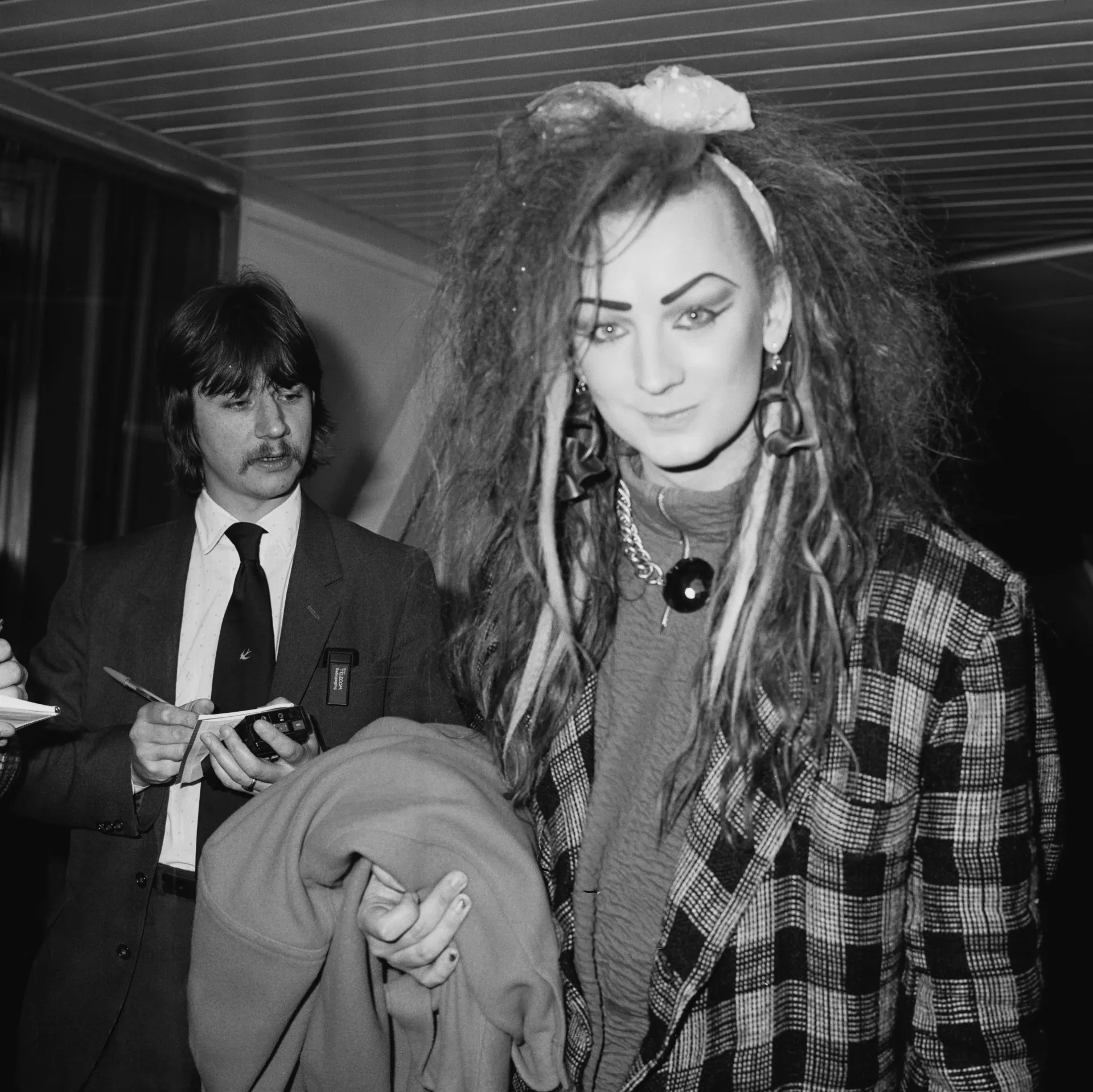Boy George nos anos 80, com maquiagem elaborada, chapéu e um visual extravagante típico do Culture Club.