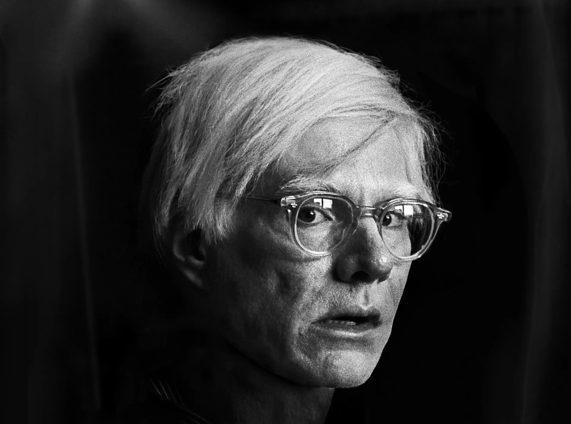 Andy Warhol posando para uma foto, refletindo sua personalidade excêntrica.
