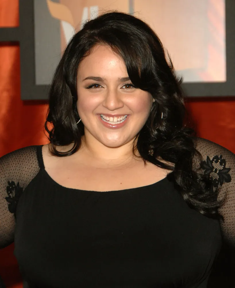 A atriz Nikki Blonsky sorrindo em um evento de tapete vermelho.