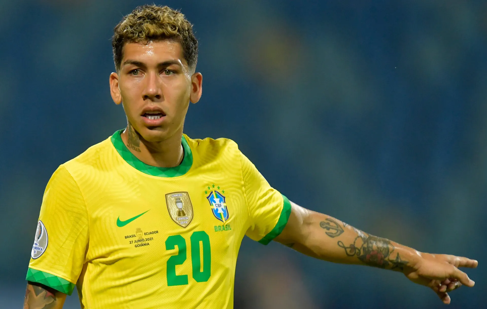 O jogador de futebol Roberto Firmino em campo, comemorando um gol.