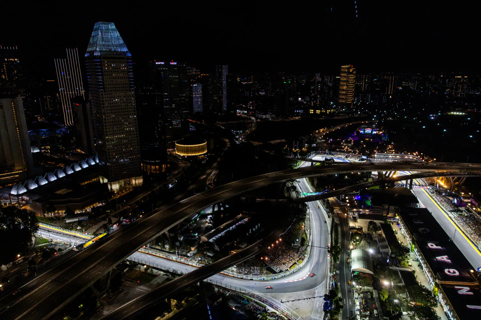 A pista de rua de Singapura iluminada à noite, com os arranha-céus da cidade ao fundo.
