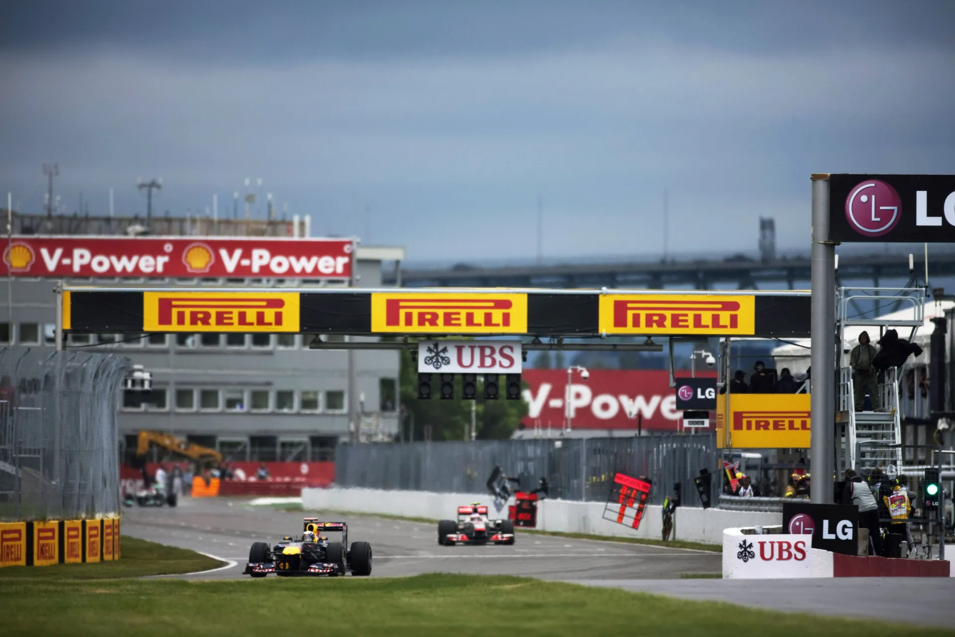Carros de F1 correndo atrás do safety car sob chuva intensa, em uma corrida longa e interrompida.