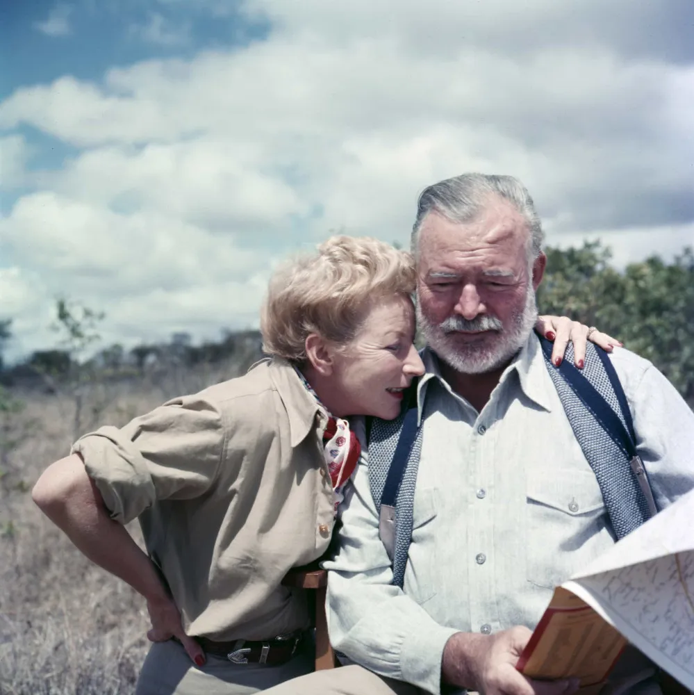 O escritor Ernest Hemingway posando ao lado de um pequeno avião, com um sorriso confiante.