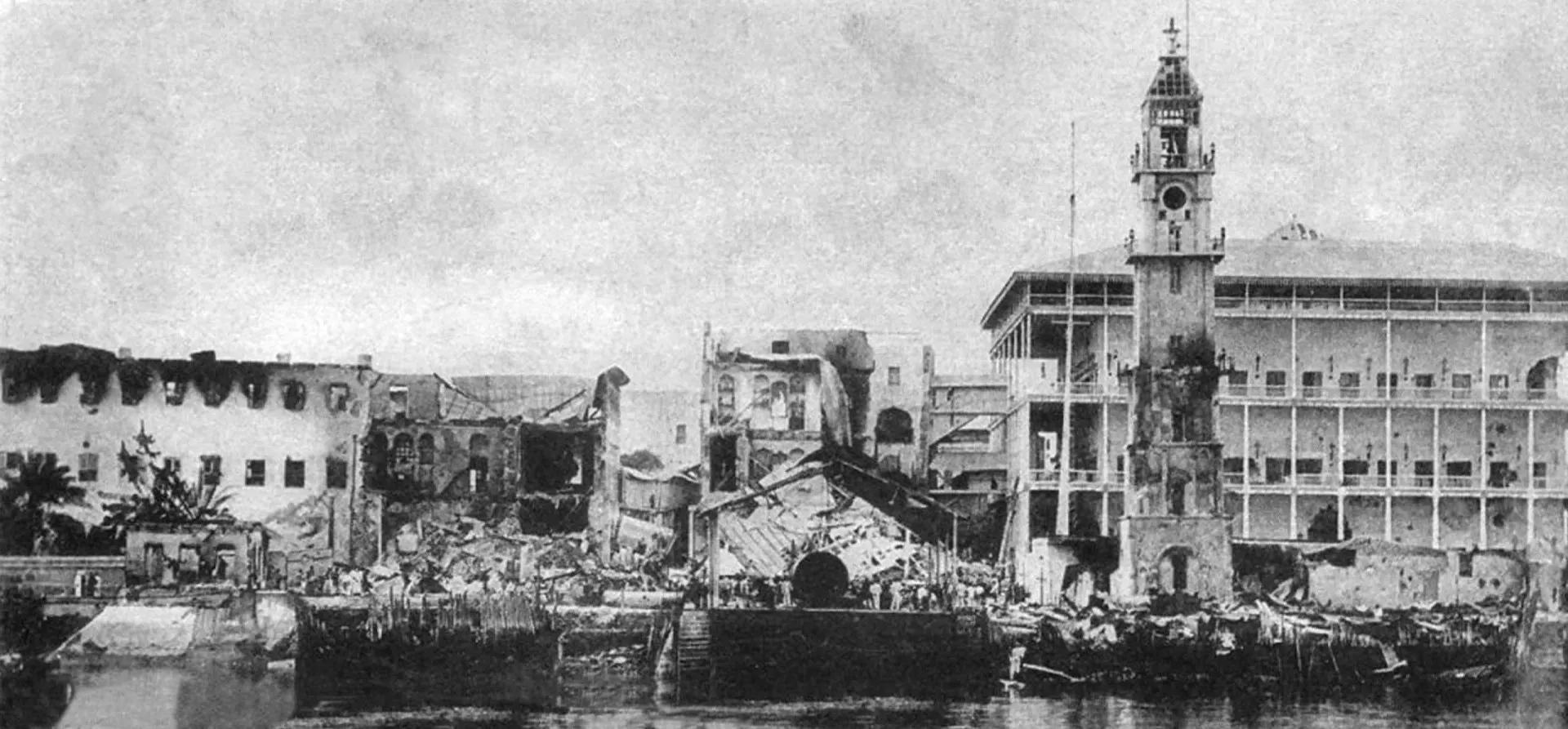 Navios de guerra britânicos disparando canhões contra um palácio em Zanzibar, com fumaça subindo.