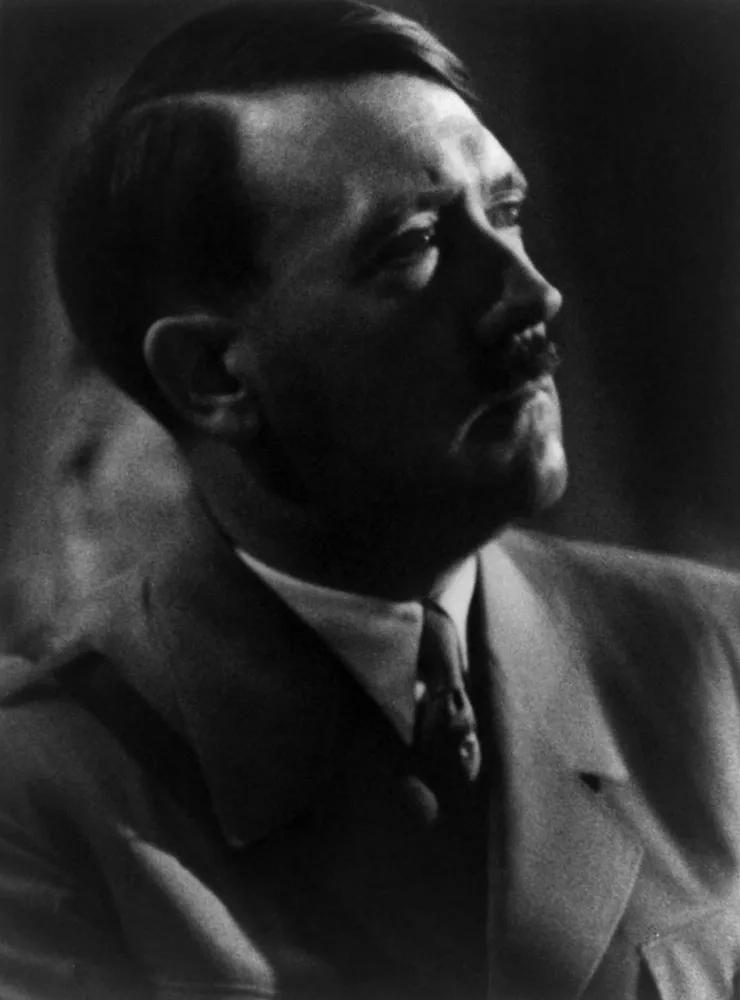 Foto em preto e branco de Adolf Hitler em um palanque, com uma expressão intensa.