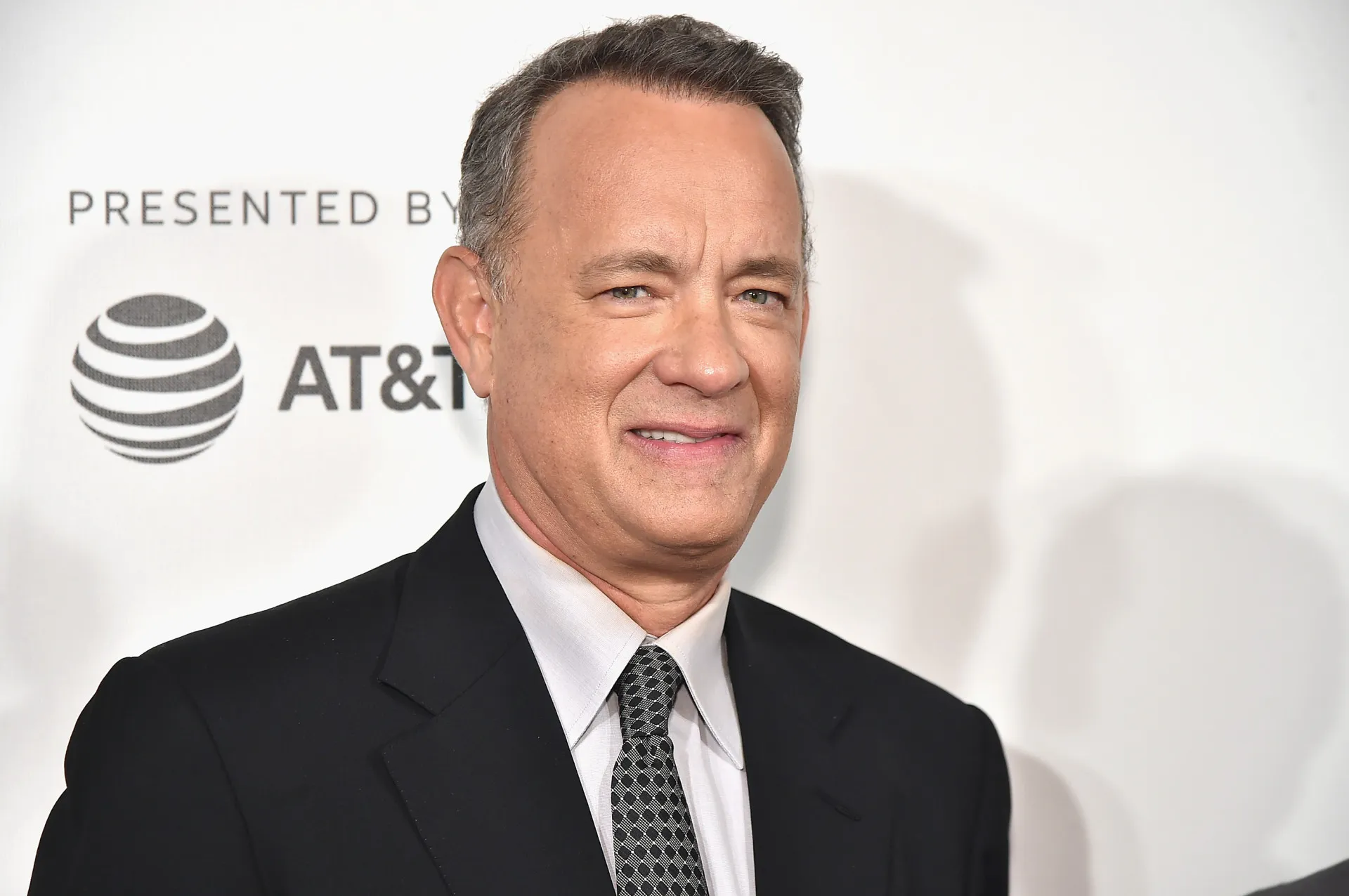 O ator Tom Hanks, conhecido por sua simpatia, sorrindo calorosamente.