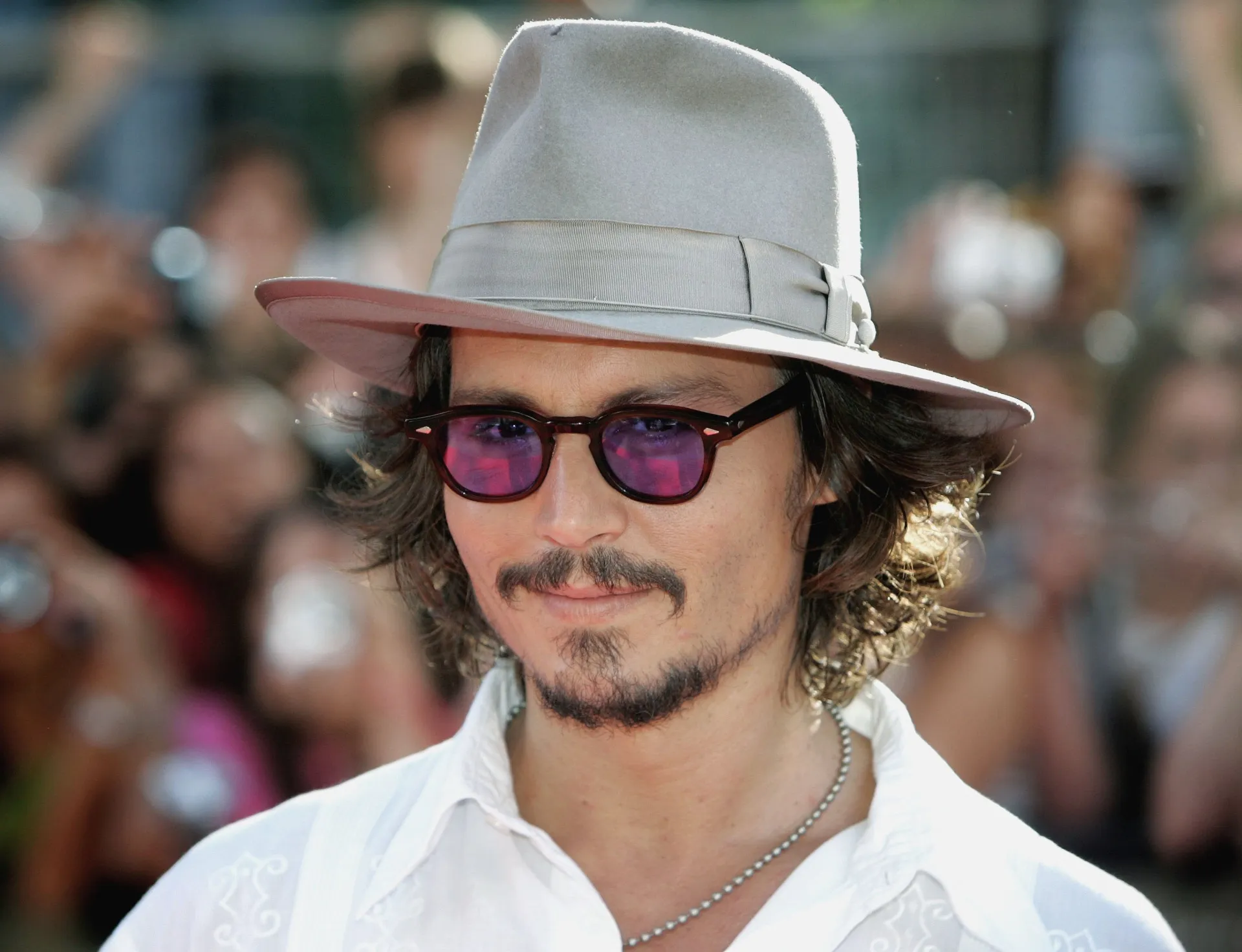 O ator Johnny Depp com seu estilo característico, incluindo óculos e chapéu.