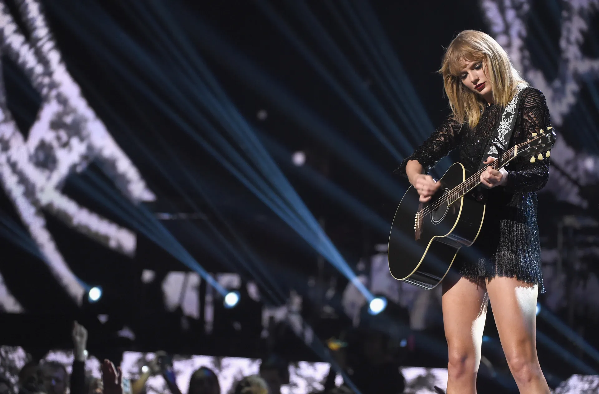 A cantora Taylor Swift tocando seu violão em uma apresentação.