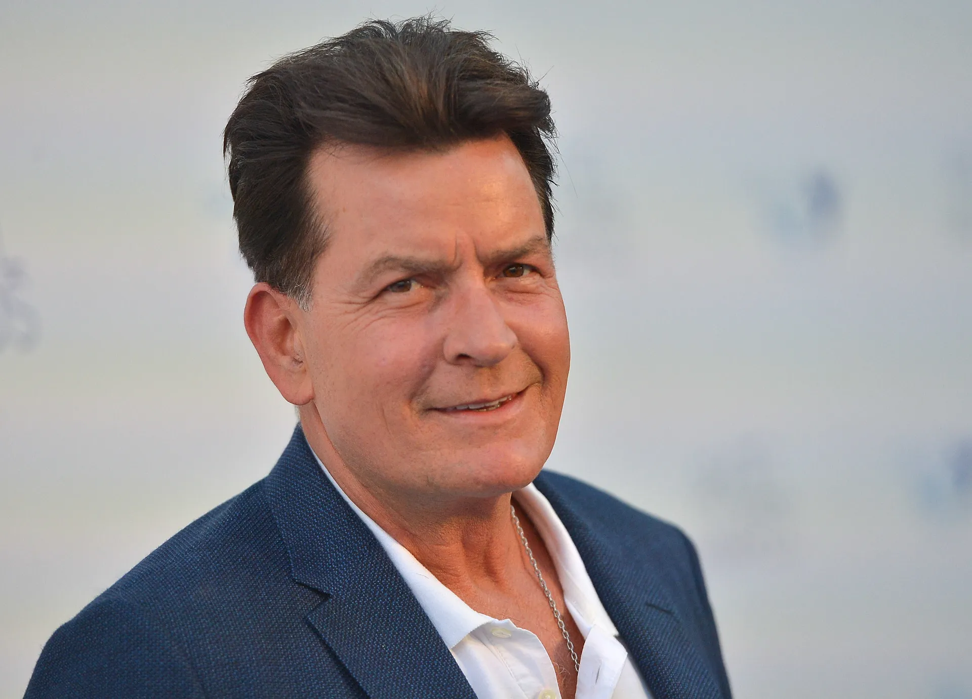 O ator Charlie Sheen com um olhar confiante e um charuto na boca.