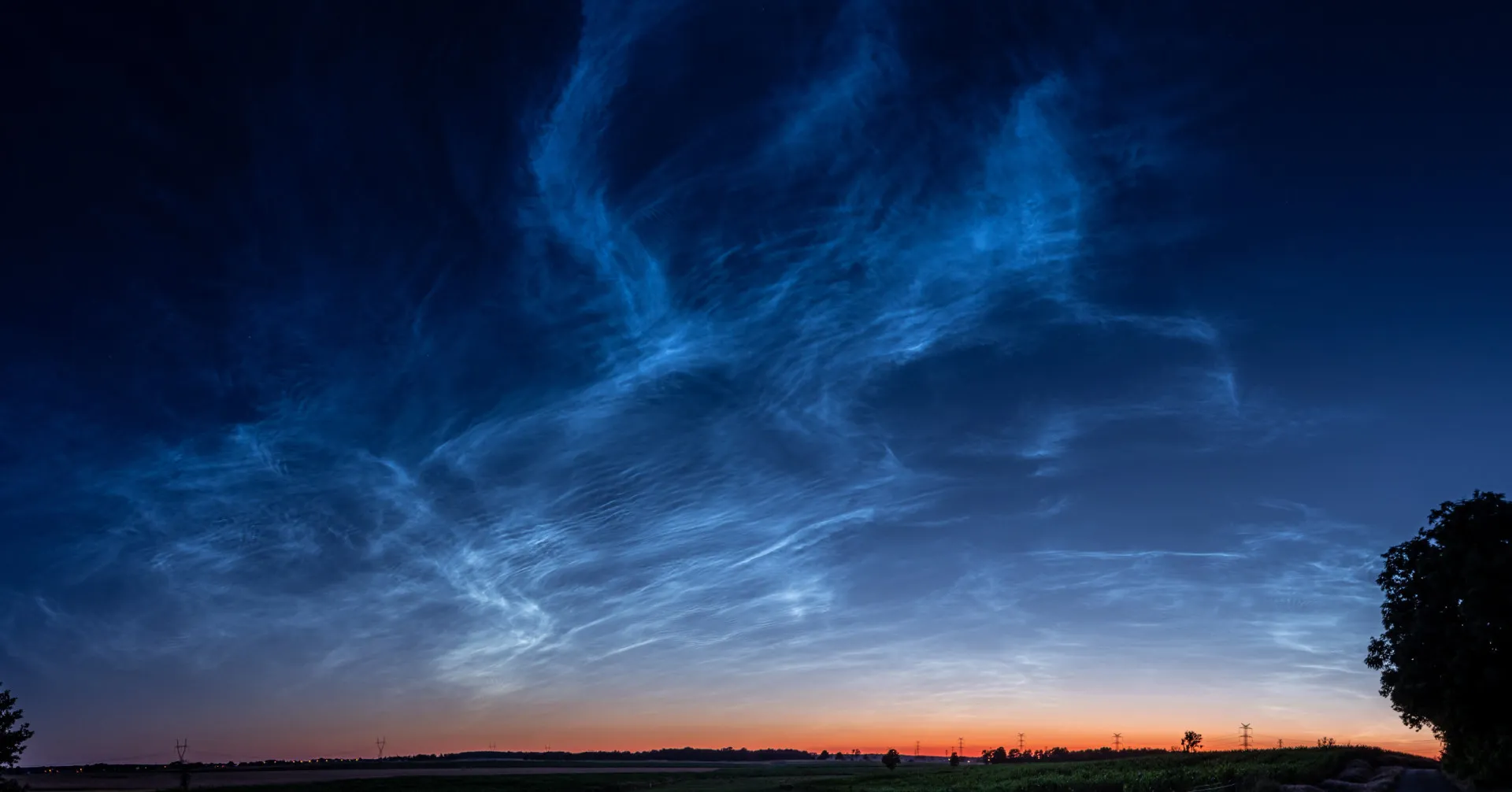 Nuvens finas e brilhantes com uma cor azul elétrica flutuando no céu escuro após o pôr do sol.