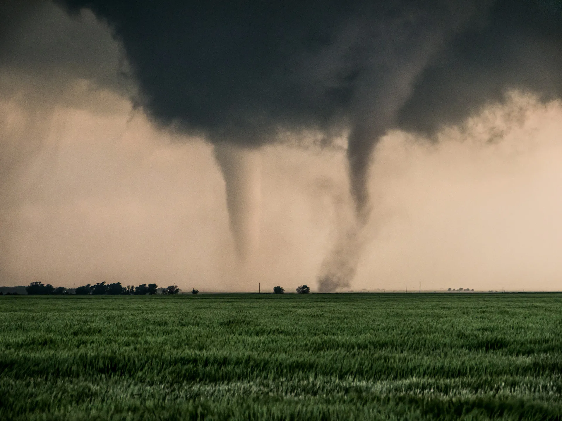 Dois tornados distintos girando lado a lado sobre um campo, ambos originados da mesma nuvem de tempestade.