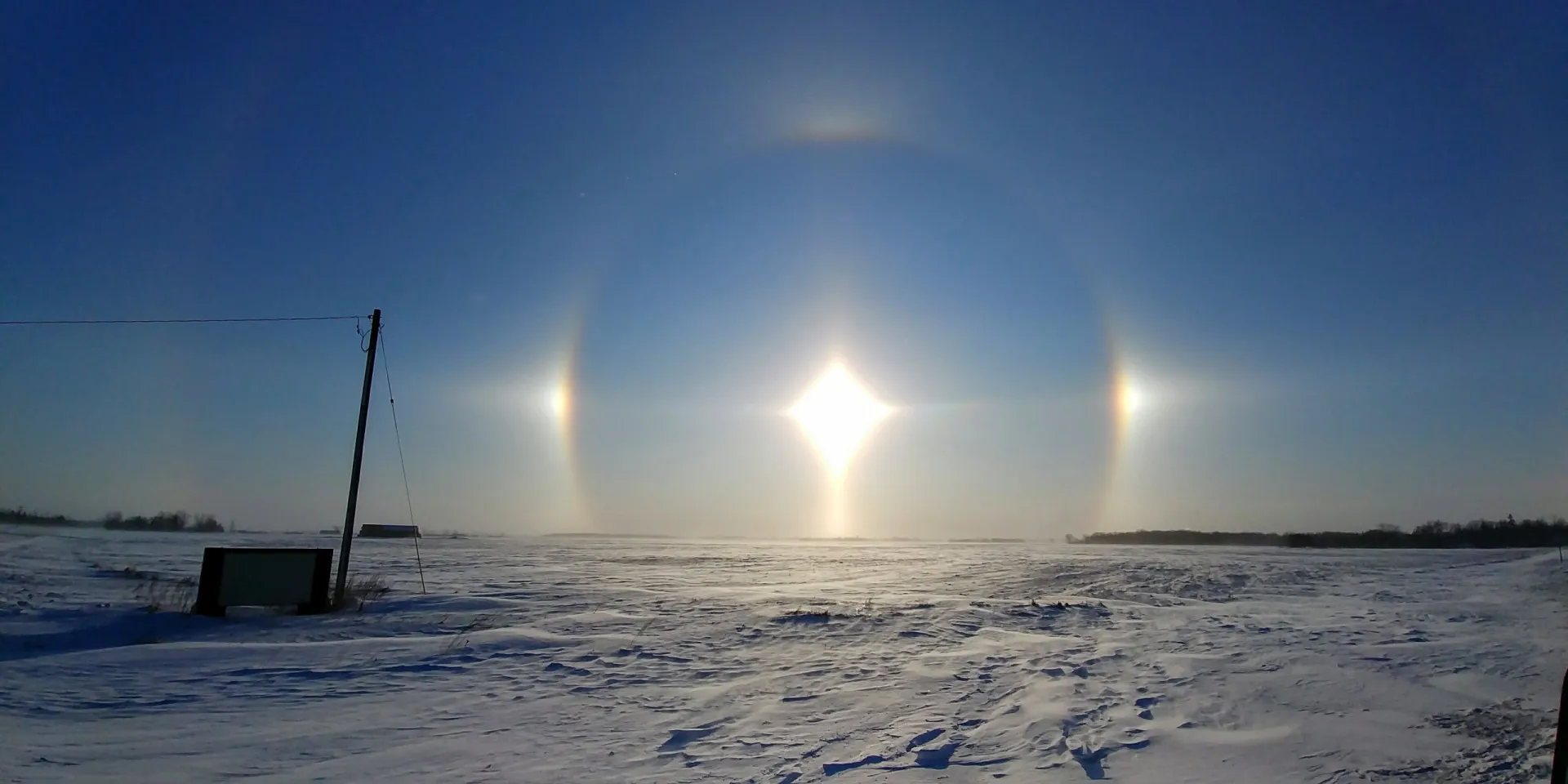 O sol no horizonte com dois pontos de luz brilhantes e coloridos em cada lado, conhecidos como sun dogs.