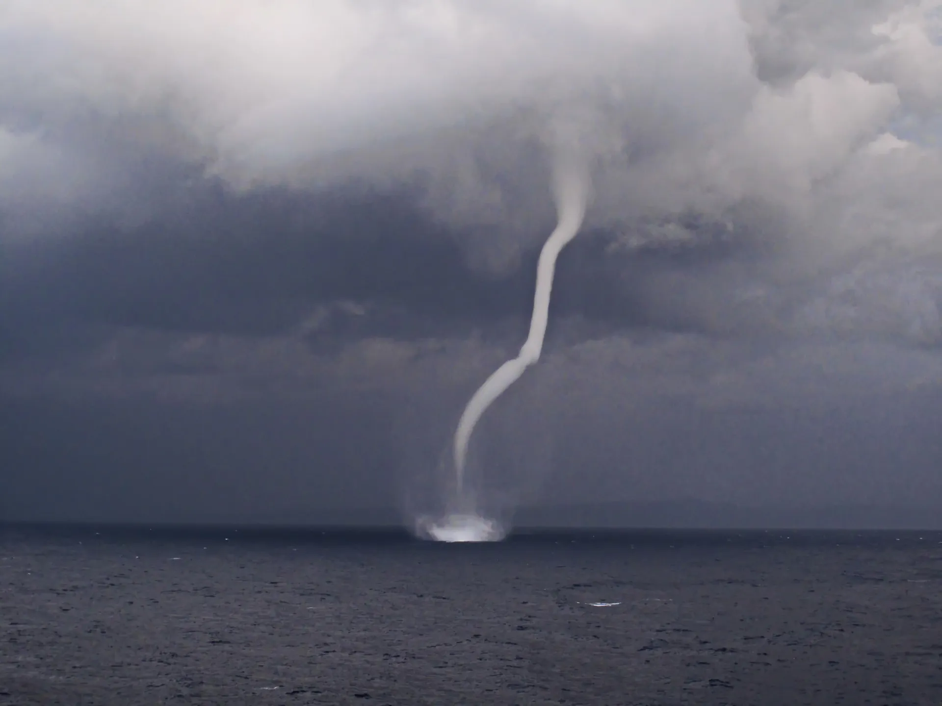 Uma tromba d'água se formando sobre o oceano, conectando a superfície da água a uma nuvem escura.