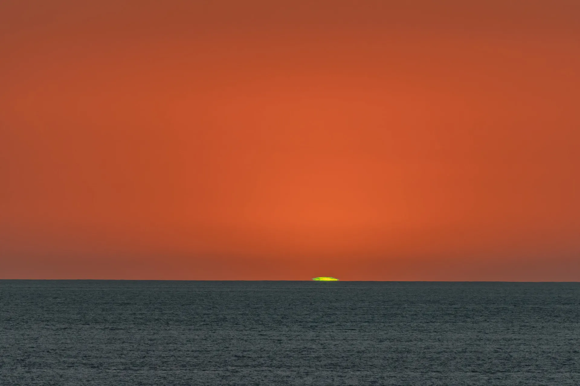 Um pequeno flash de luz verde brilhante visível no horizonte exatamente no momento em que o sol se põe no oceano.