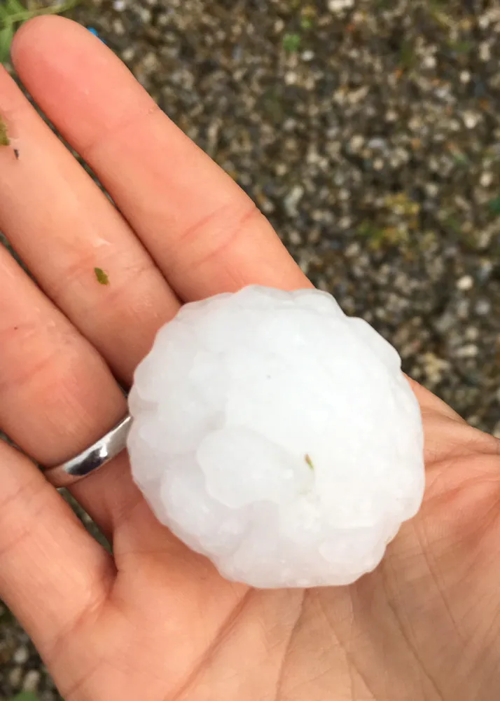 Um carro com o para-brisa completamente estilhaçado por grandes pedras de granizo.
