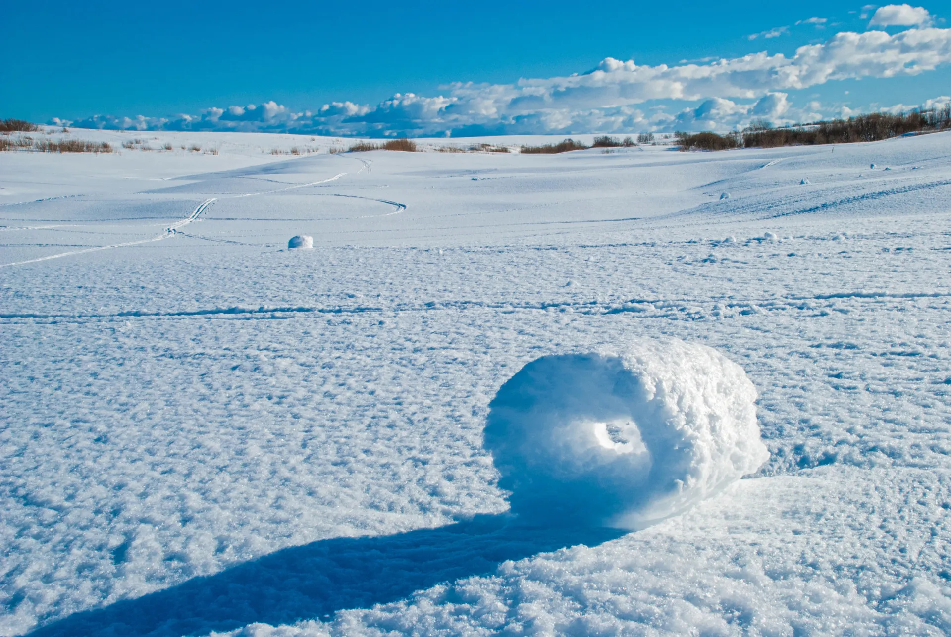 Vários rolos de neve de diferentes tamanhos espalhados por um campo nevado.