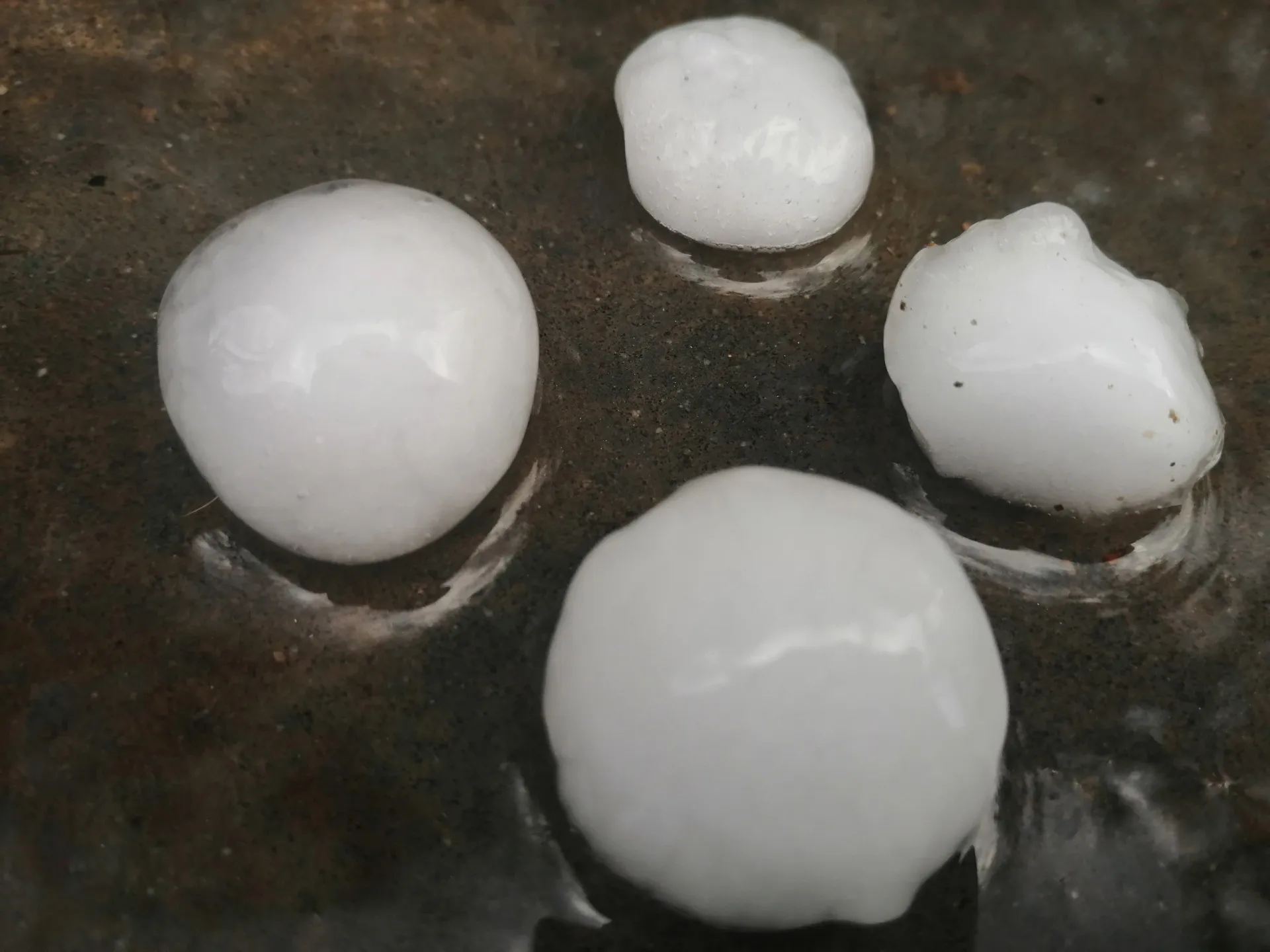 Uma mão segurando uma pedra de granizo enorme e irregular, do tamanho de uma bola de beisebol.