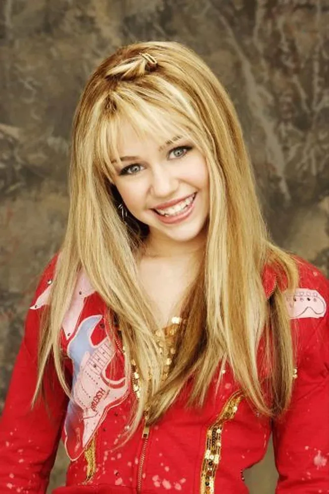 Miley Cyrus como a personagem Hannah Montana no palco, com um visual chamativo e cheio de brilho.