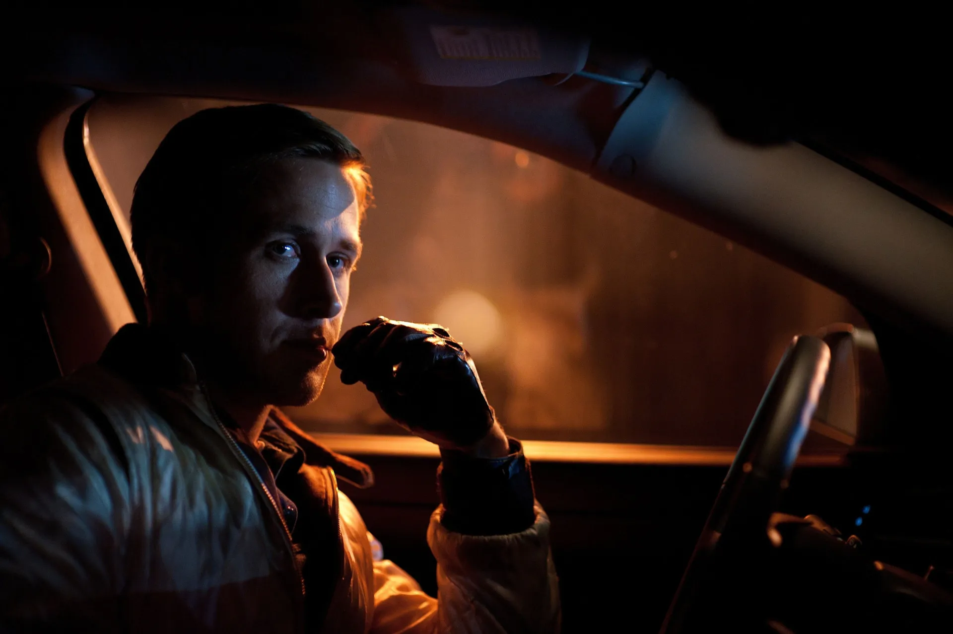 Ryan Gosling como o motorista silencioso no filme Drive, olhando intensamente pelo retrovisor.