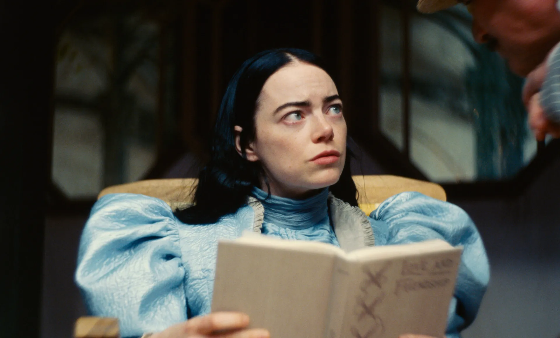 Emma Stone como Bella Baxter em 'Pobres Criaturas', com um olhar curioso e desafiador em um cenário surreal.
