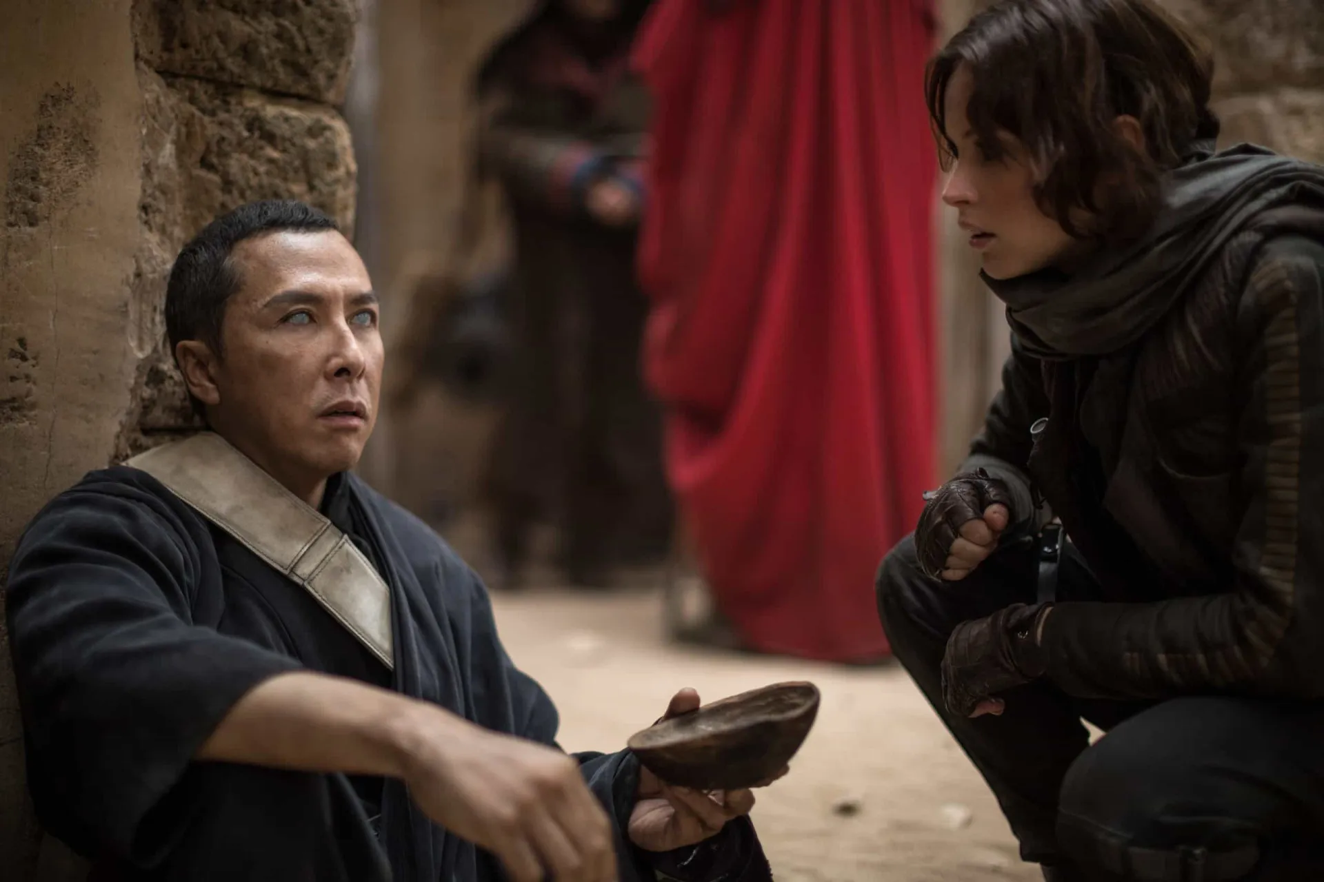 Jyn Erso e Cassian Andor se abraçam em uma praia enquanto uma explosão acontece ao fundo em 'Rogue One'.