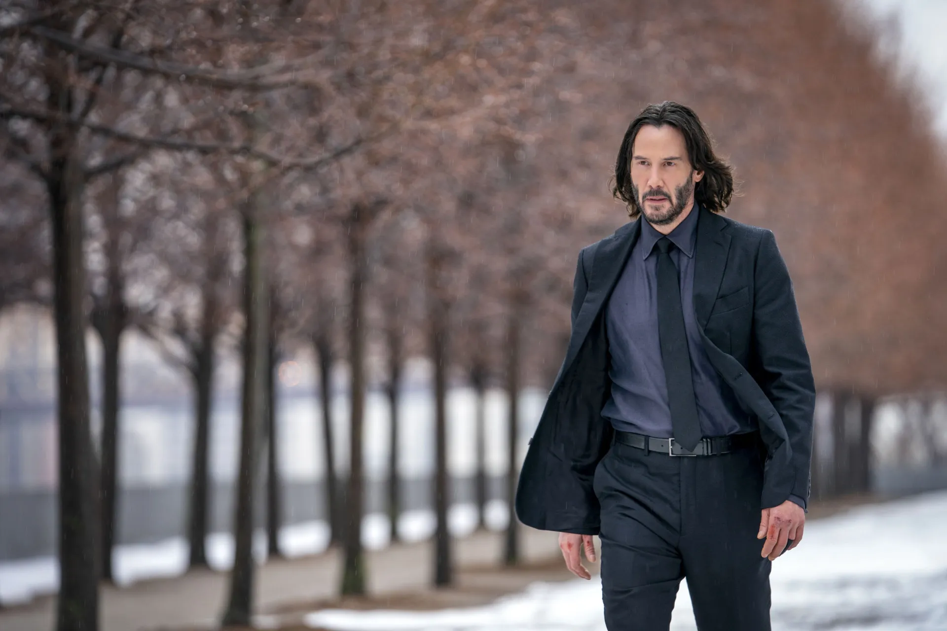 Keanu Reeves mais velho como John Wick, com cabelo comprido, barba e um olhar focado e letal.