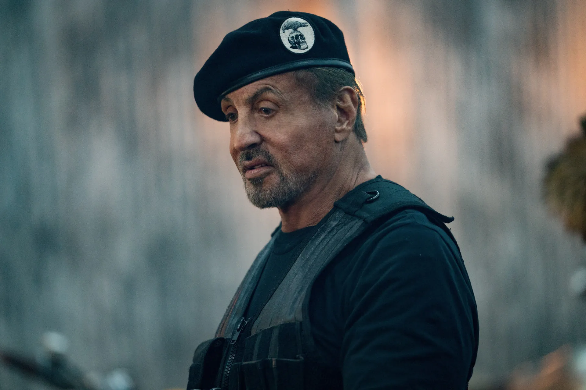 Sylvester Stallone mais velho, de terno, com um charuto na boca, exibindo um ar de poder.