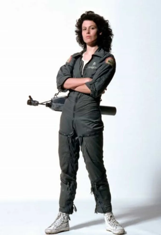 Sigourney Weaver jovem como Ellen Ripley na franquia 'Alien', com cabelo cacheado e olhar determinado.