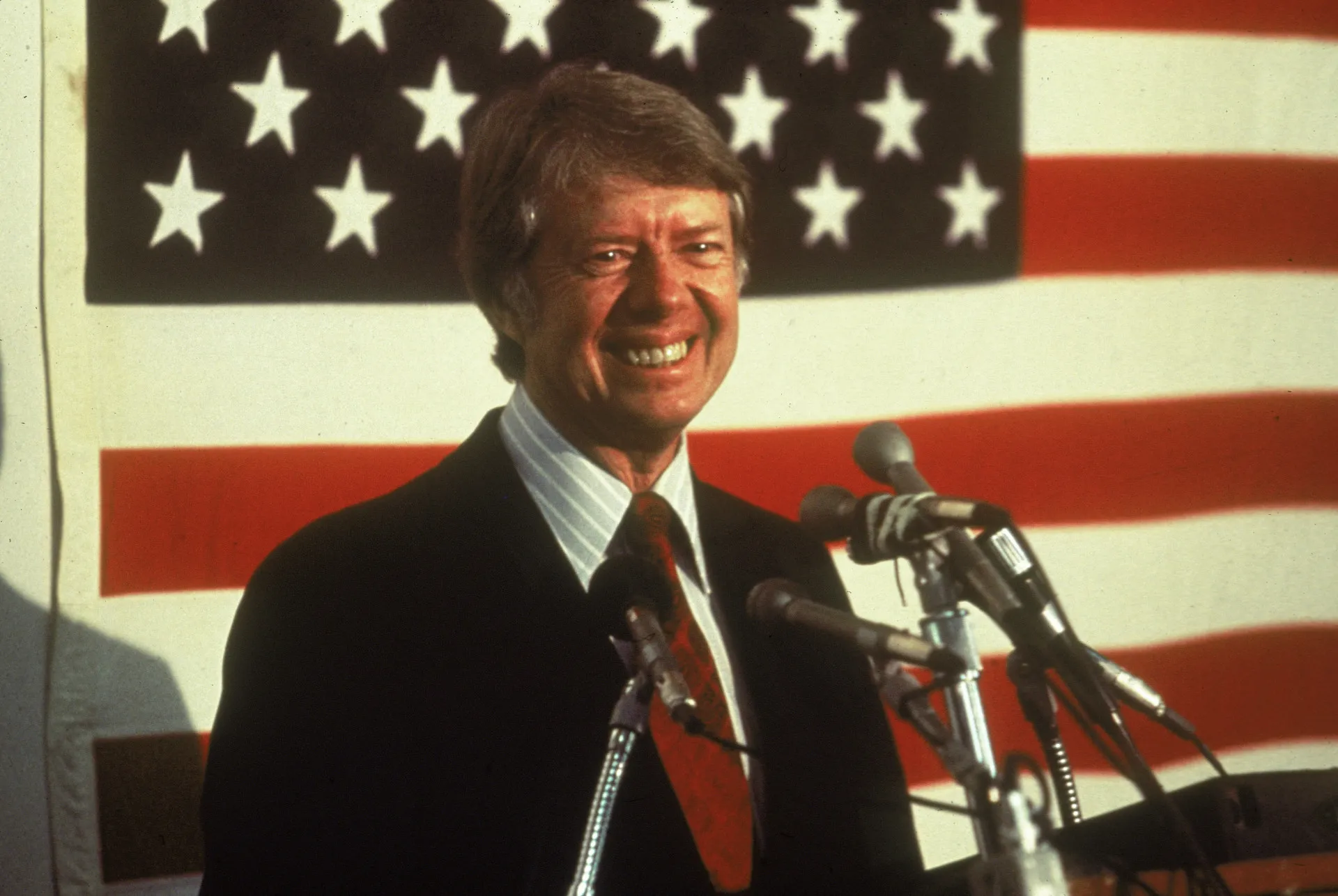 Jimmy Carter durante um discurso, com a bandeira dos EUA ao fundo.