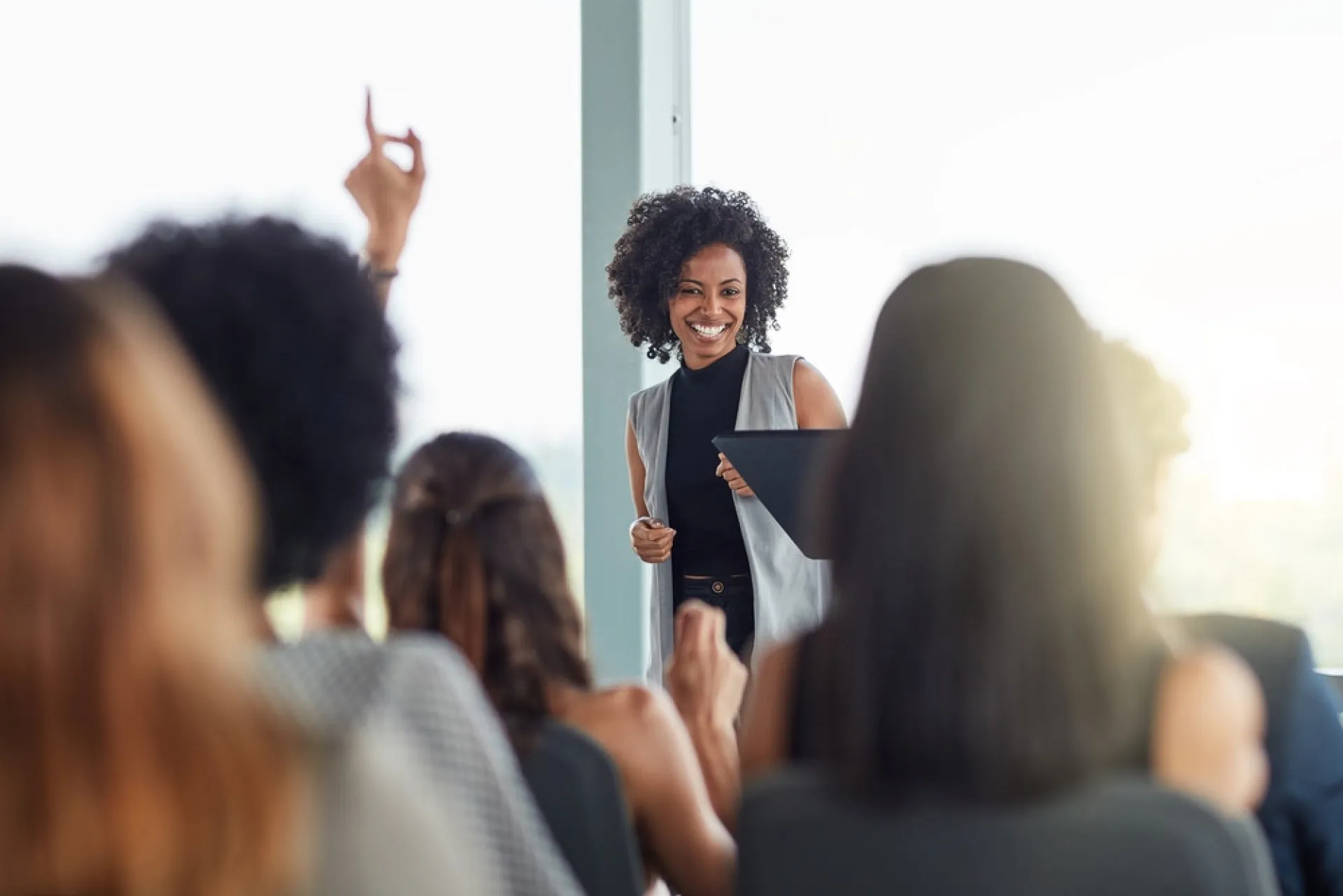 Grupo de adultos em uma sala de aula, levantando as mãos e participando ativamente de uma palestra.