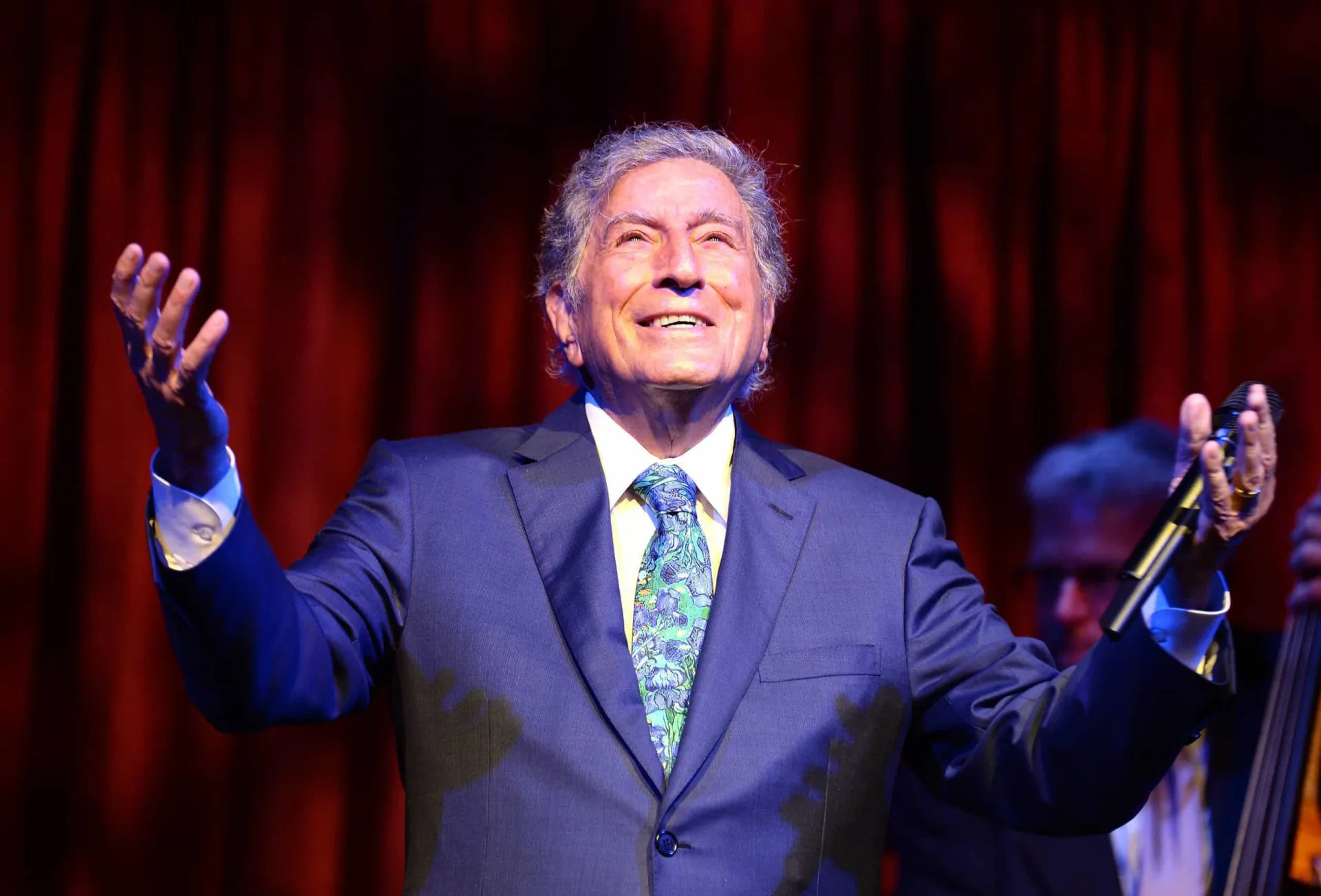 O cantor Tony Bennett sorrindo no palco, ao lado de Lady Gaga.