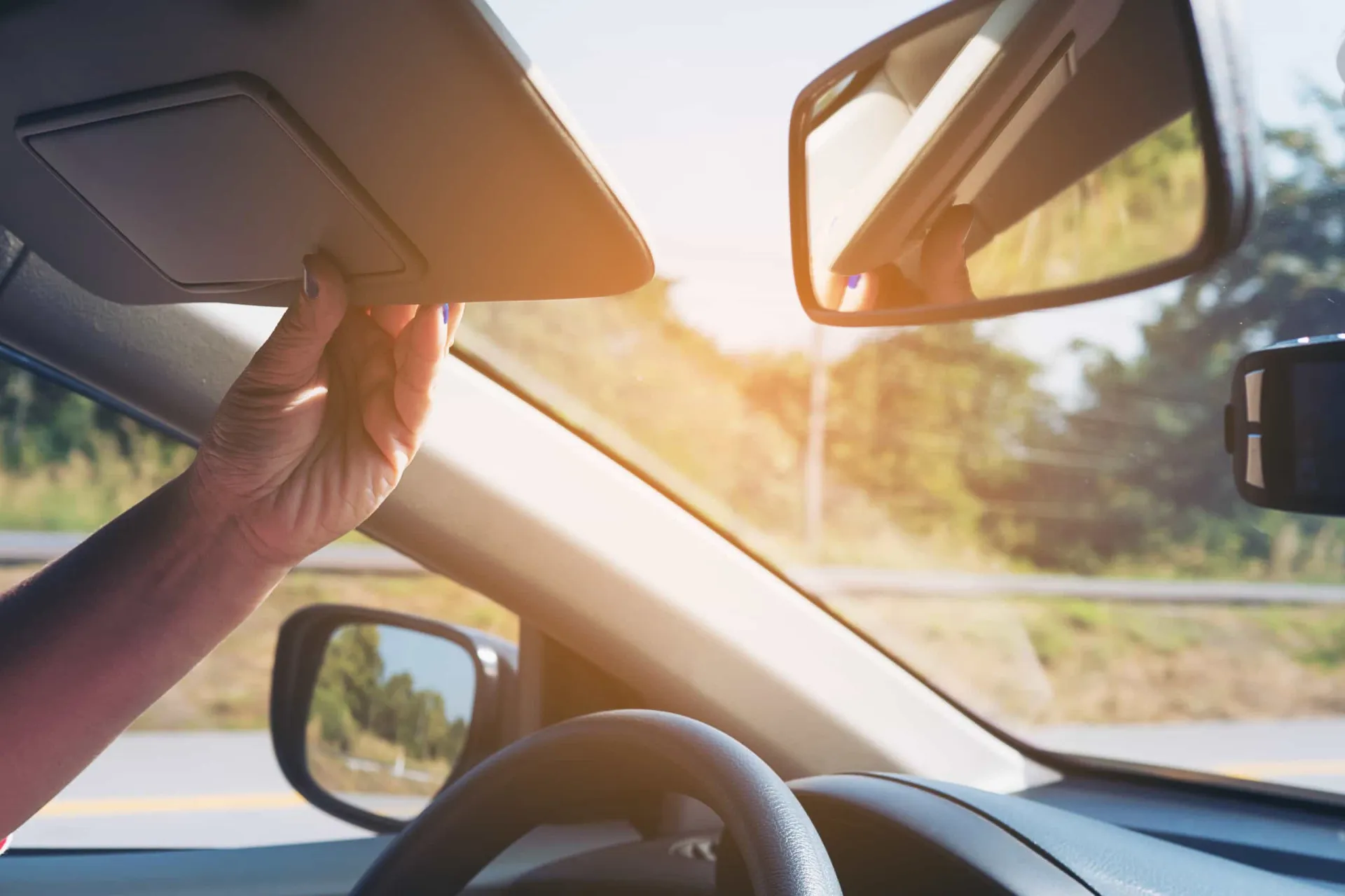 Mão de uma pessoa pegando a chave do carro que estava escondida no quebra-sol do veículo.
